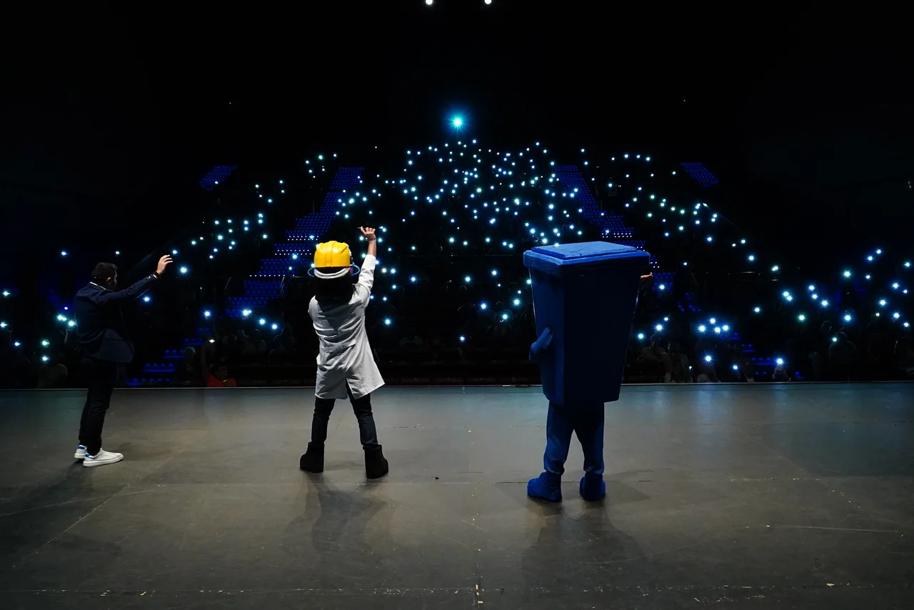 Auditório do SST Summit com o público sentado, iluminação de palco e mascotes do evento